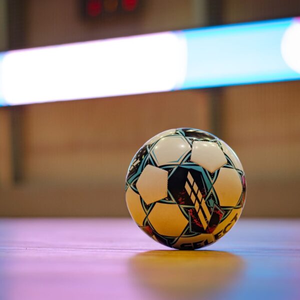 Close-up of a soccer ball on a gym floor with blurred background lights.