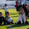 A group of happy children and their coach enjoy a sunny day on the football field.