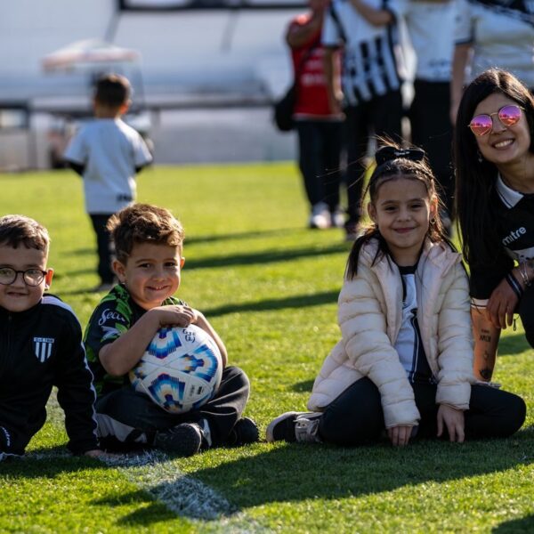 A group of happy children and their coach enjoy a sunny day on the football field.