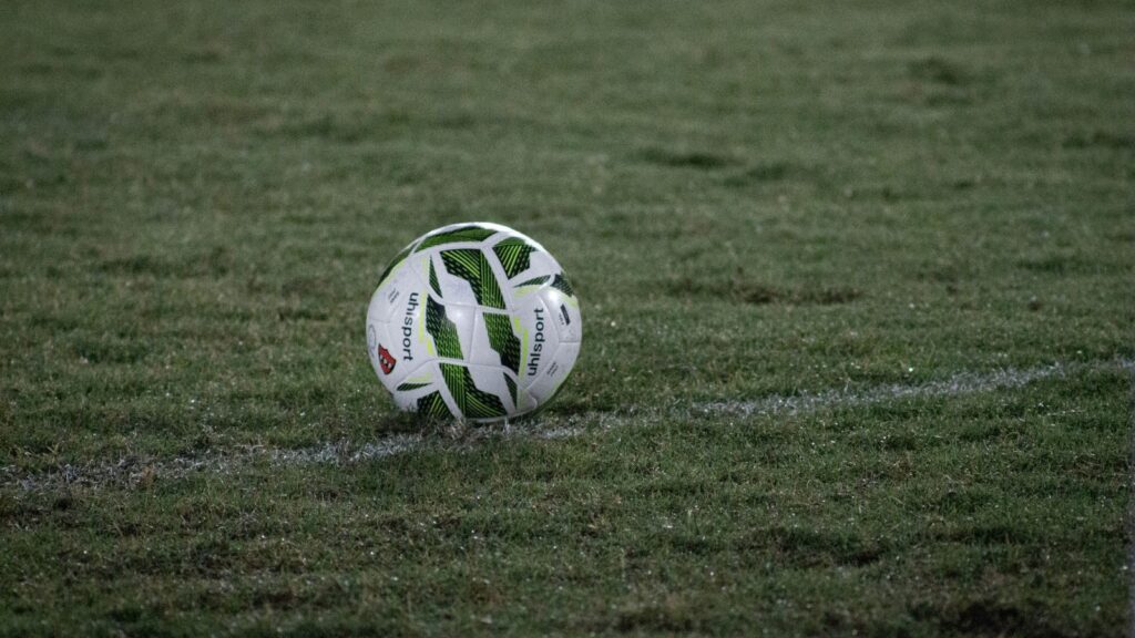 A soccer ball resting on a grass field, captured during nightfall with visible dew.