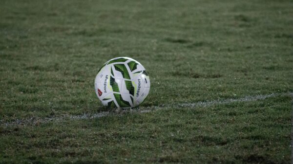 A soccer ball resting on a grass field, captured during nightfall with visible dew.