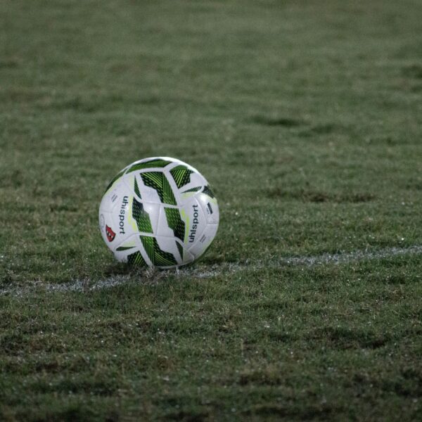 A soccer ball resting on a grass field, captured during nightfall with visible dew.