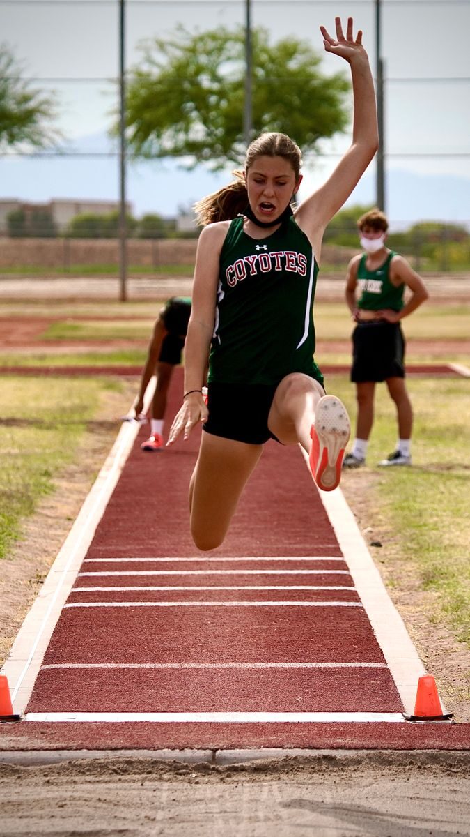 Athlete performing long jump outdoors on track field during daytime event