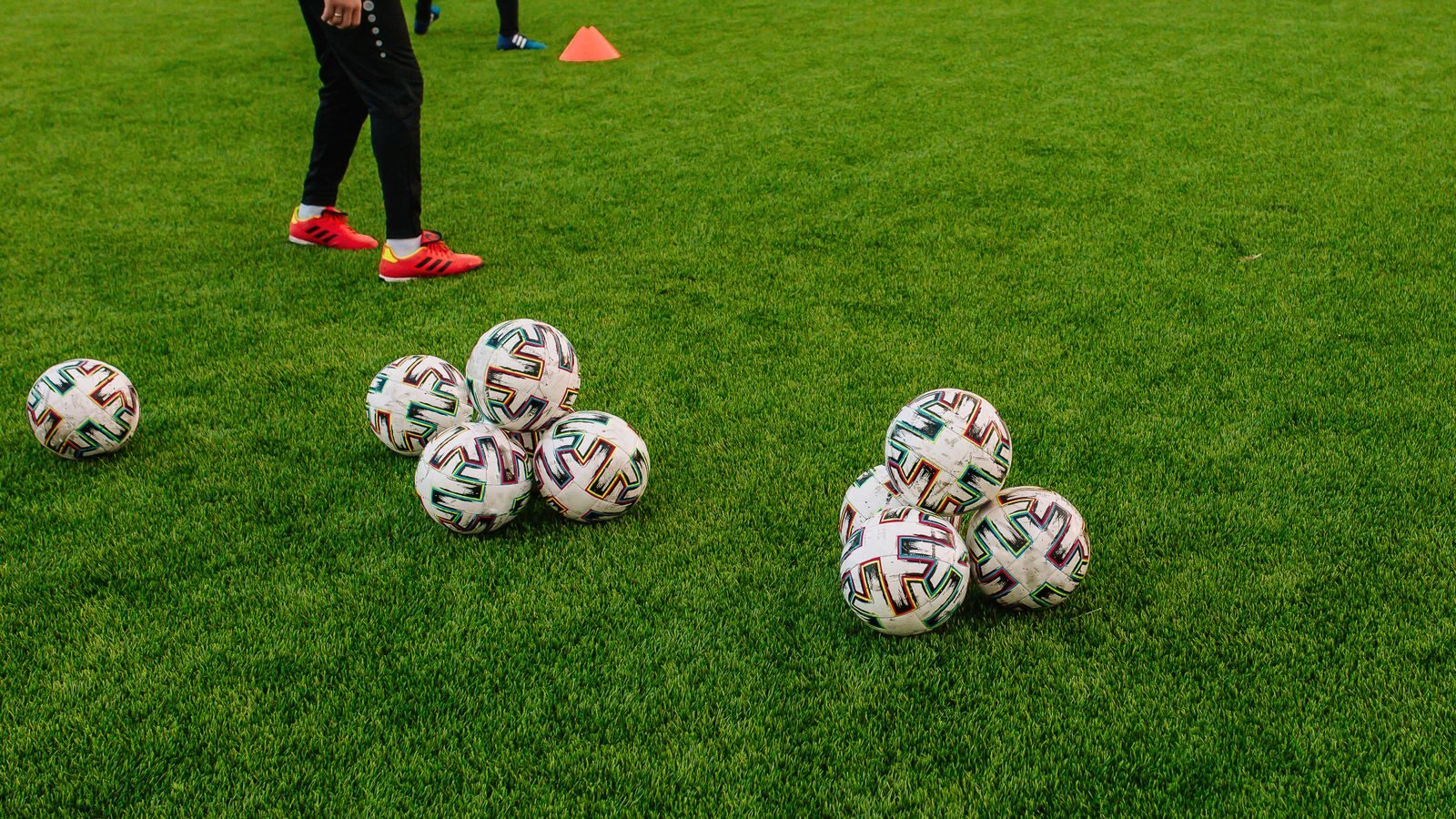 Pile of soccer balls on a green field with a person preparing for training session.