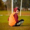 Boy in hoodie seated on a football field in Antalya, gazing over shoulder.