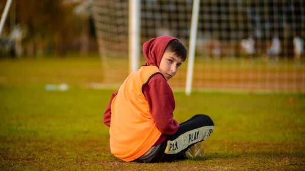 Boy in hoodie seated on a football field in Antalya, gazing over shoulder.