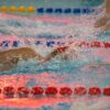 Swimmers in action during a competitive swimming event with vibrant reflections.