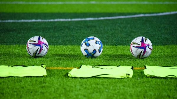 Three soccer balls and training bibs on a lush green field in Rawalpindi, Pakistan.