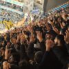 Energetic fans with raised hands in a stadium, supporting their soccer team with enthusiasm.