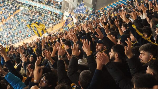 Energetic fans with raised hands in a stadium, supporting their soccer team with enthusiasm.
