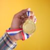 Close-up of a hand holding a gold medal with a colorful ribbon, symbolizing victory and achievement.
