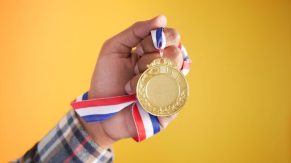 Close-up of a hand holding a gold medal with a colorful ribbon, symbolizing victory and achievement.