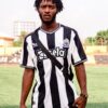 African man in a striped football jersey standing on a sports field during daylight.