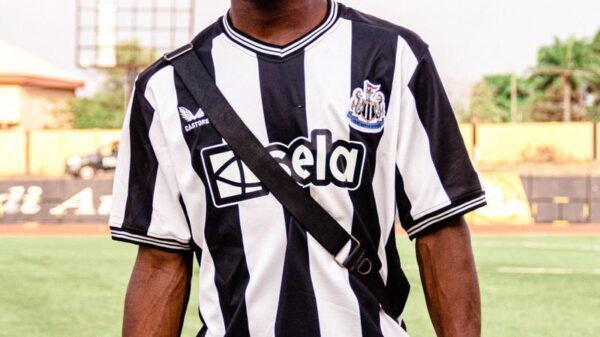 African man in a striped football jersey standing on a sports field during daylight.