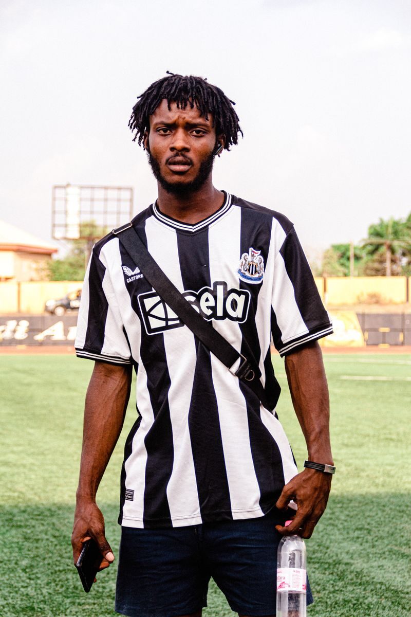 African man in a striped football jersey standing on a sports field during daylight.