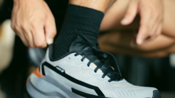 Close-up of a man tying a modern athletic shoe on a reflective surface indoors.