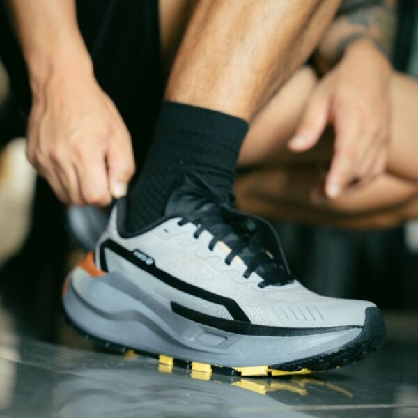 Close-up of a man tying a modern athletic shoe on a reflective surface indoors.