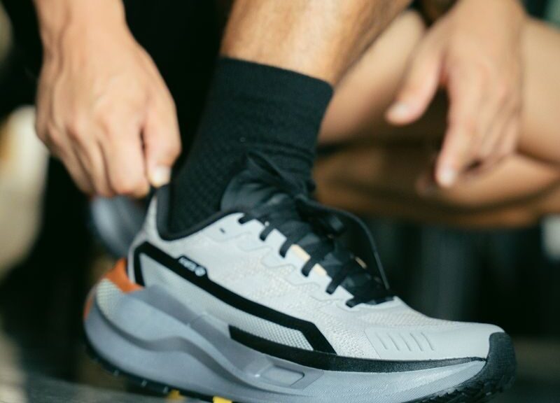 Close-up of a man tying a modern athletic shoe on a reflective surface indoors.