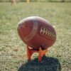 A detailed view of an American football resting on a grass field during daylight.