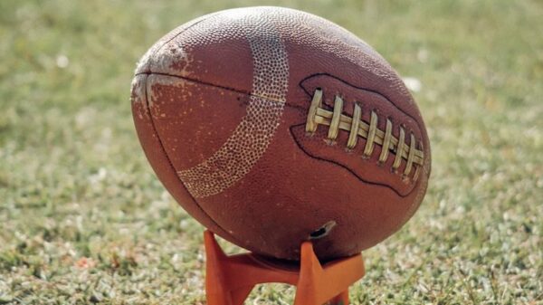 A detailed view of an American football resting on a grass field during daylight.