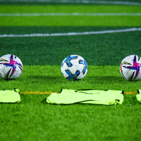 Three soccer balls and training bibs on a lush green field in Rawalpindi, Pakistan.