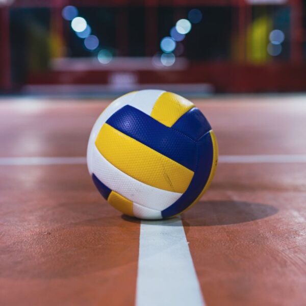 Close-up of a volleyball resting on the line of an indoor court, focus on the ball.