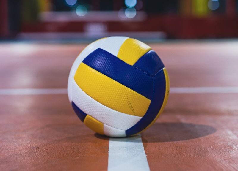 Close-up of a volleyball resting on the line of an indoor court, focus on the ball.