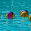 Vibrant water polo balls drifting on clear turquoise water under the sun.