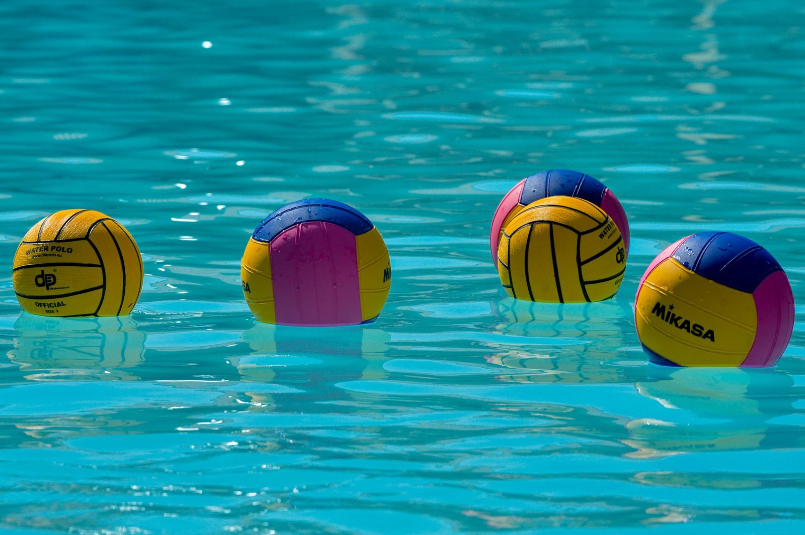 Vibrant water polo balls drifting on clear turquoise water under the sun.