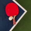 A red table tennis paddle and ball on a blue and green table surface.