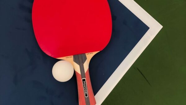A red table tennis paddle and ball on a blue and green table surface.