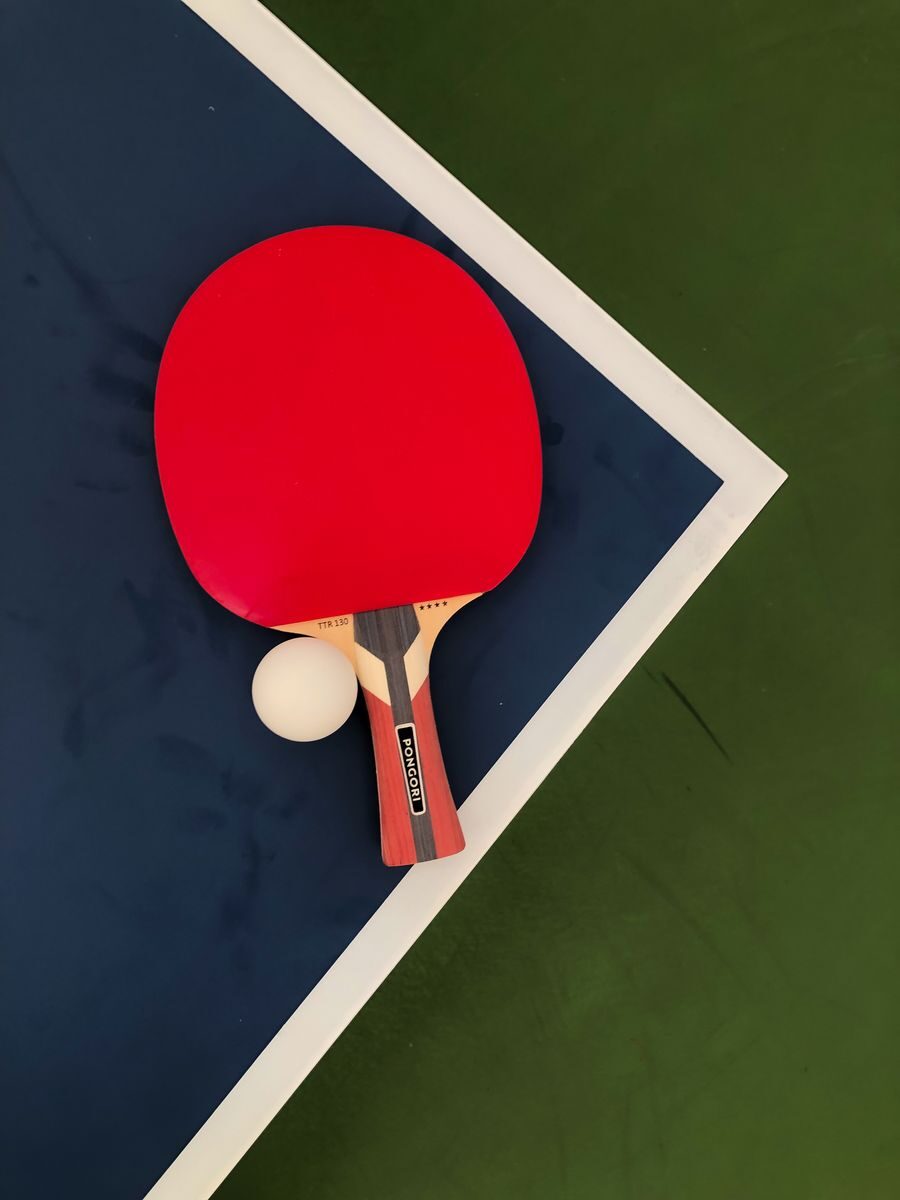 A red table tennis paddle and ball on a blue and green table surface.