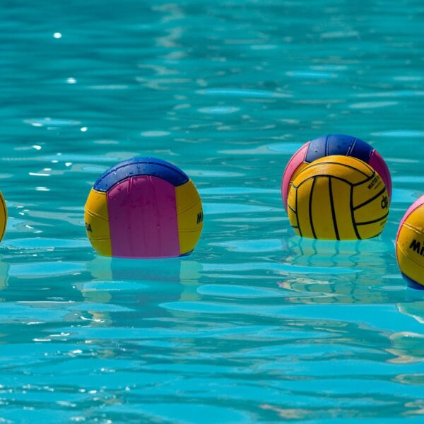 Vibrant water polo balls drifting on clear turquoise water under the sun.