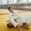 Two male adults engaged in judo practice on a dojo mat, showcasing martial arts technique.