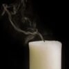 Burnt out white thick wax candle faded with smoke on black background of studio