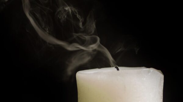 Burnt out white thick wax candle faded with smoke on black background of studio