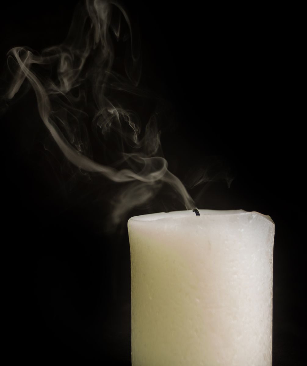 Burnt out white thick wax candle faded with smoke on black background of studio